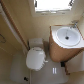 Bagno per camper o caravan con wc orientabile, doccia e mobile lavandino arrotondato in legno.